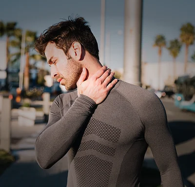 Athlete holding his neck in discomfort outdoors, representing sports physical therapy care for chronic pain.