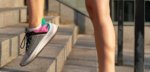Close-up of a runner's foot in a grey and pink sneaker stepping up concrete outdoor stairs.