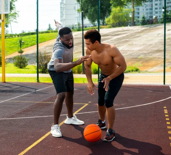 Two athletes playing basketball on an outdoor court representing sports physical therapy rehab and performance training in DFW.